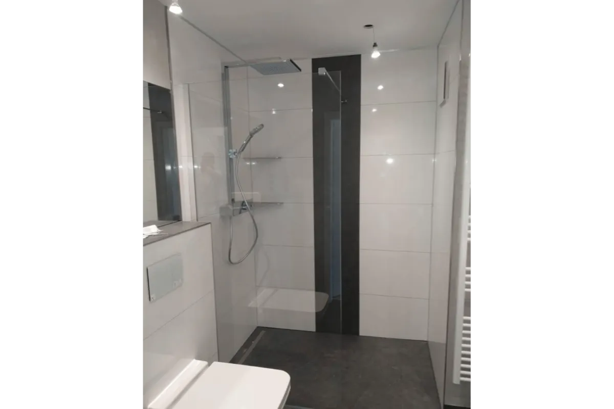 Modernisiertes Bad mit bodenebener Glasdusche und weißen Wandfliesen